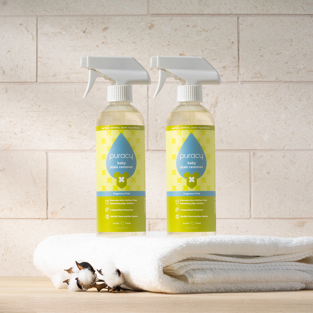 Two bottles of Baby Stain Remover on folded white towels with cotton flowers.
