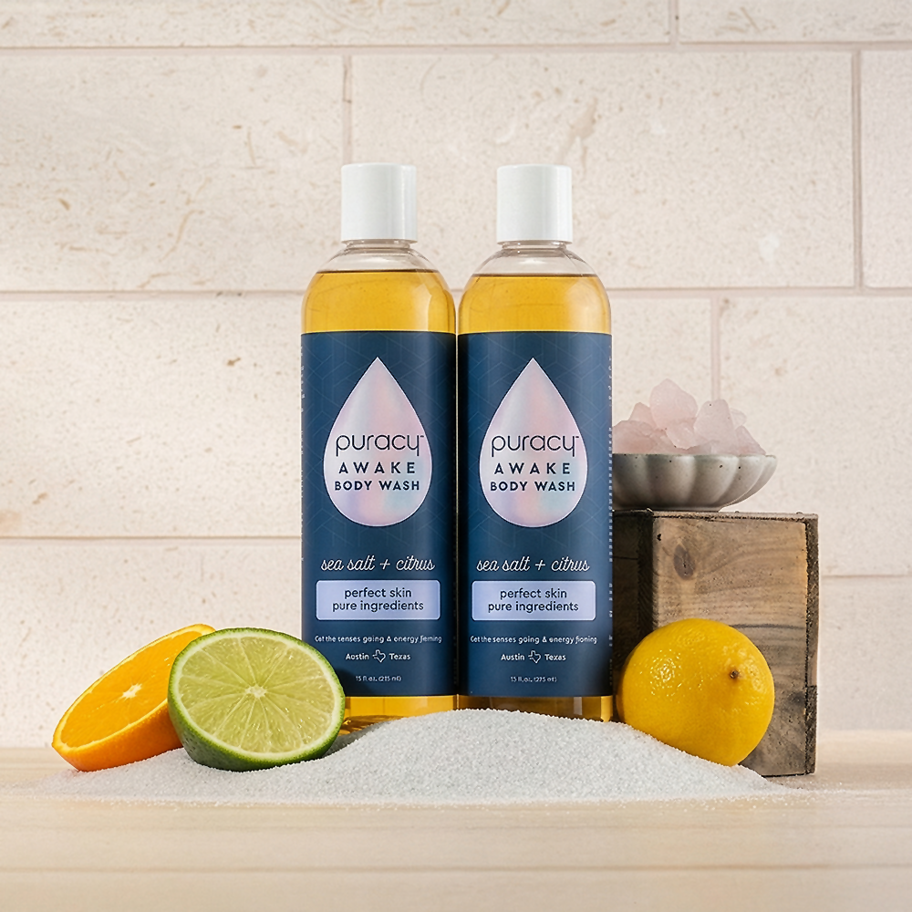 Two Body Wash (Acidified, PH Balanced) bottles with citrus fruits, sea salt, and pink salt on a counter.