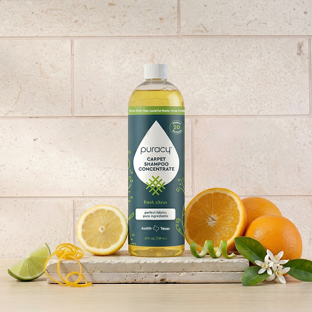 A bottle of Puracy Carpet & Upholstery Shampoo with citrus fruits on wood, tiled wall behind.