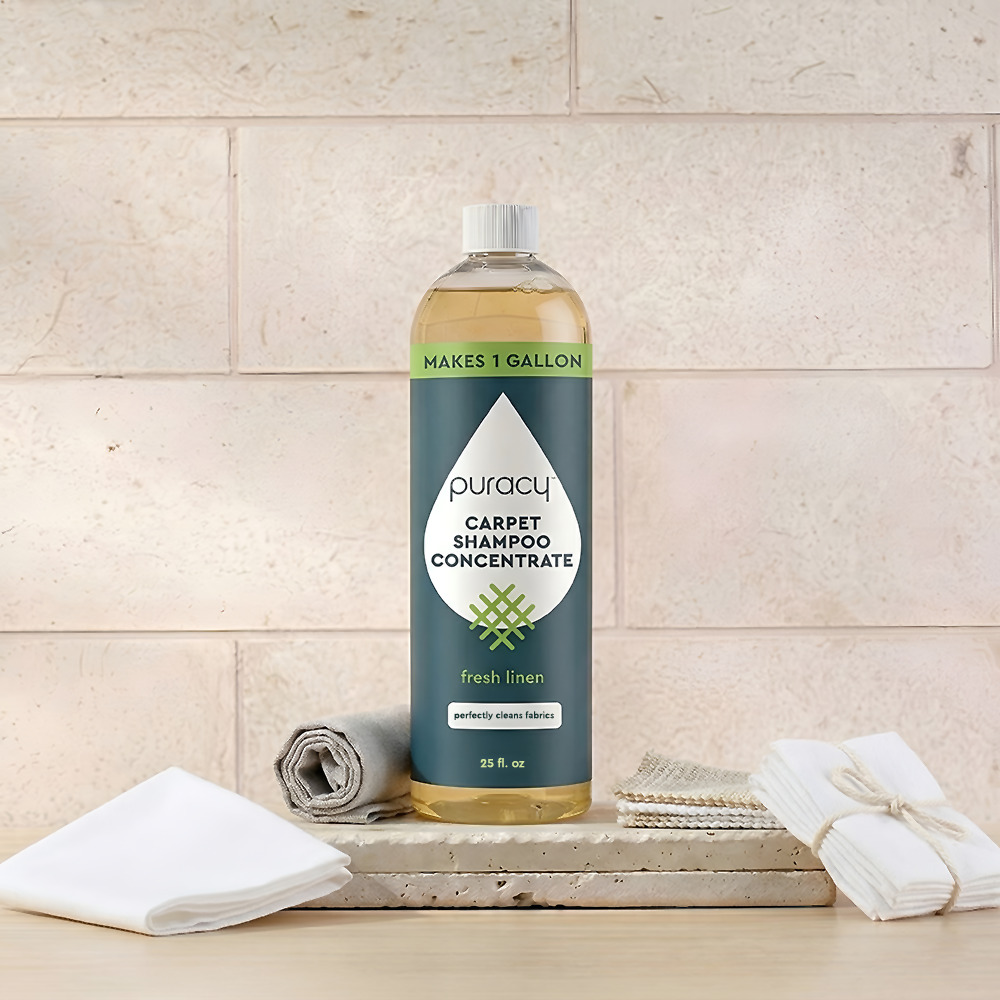 A bottle of Puracy Carpet & Upholstery Shampoo sits with towels and a scrub brush.