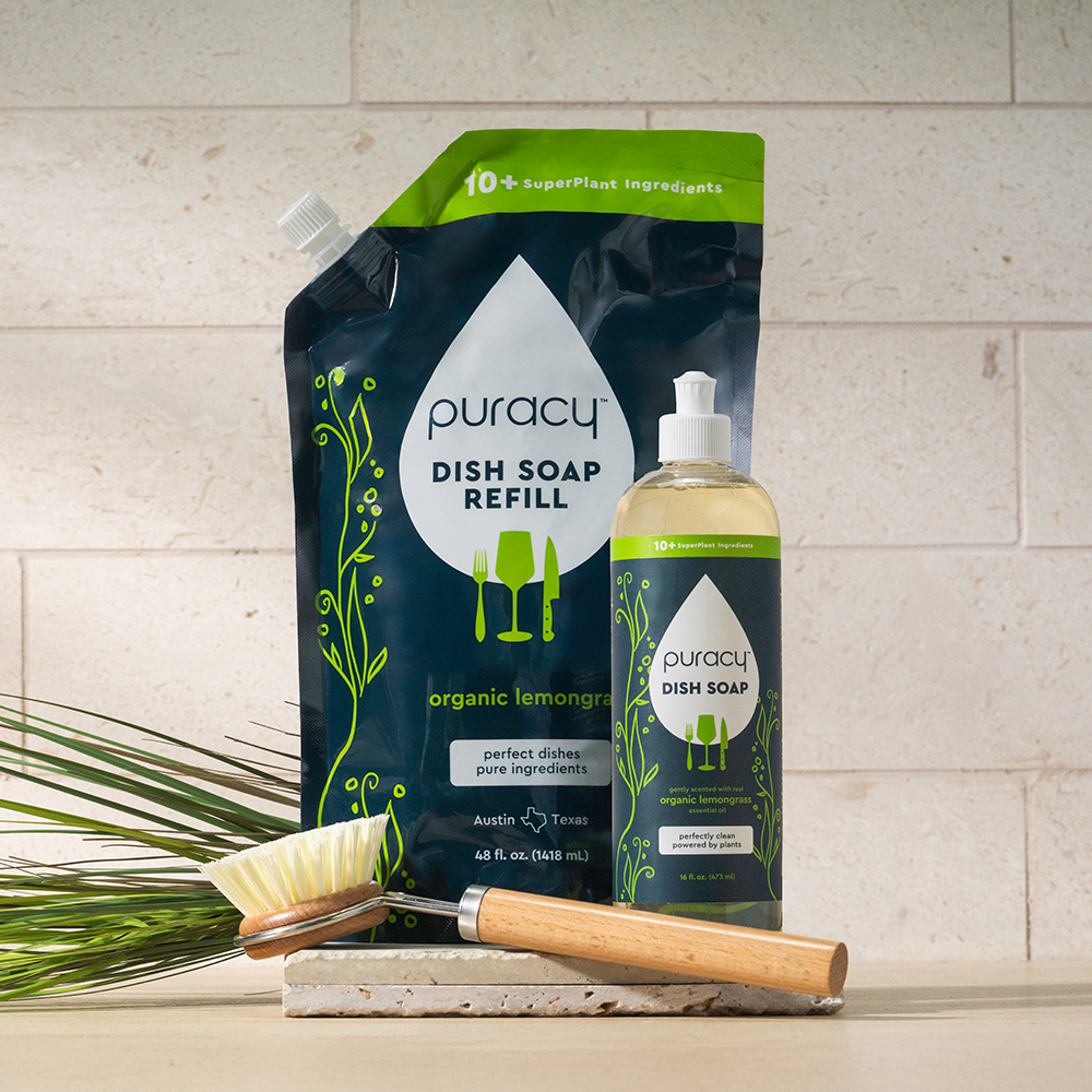 Puracy Dish Soap with bottle, brush, and plant on marble surface.