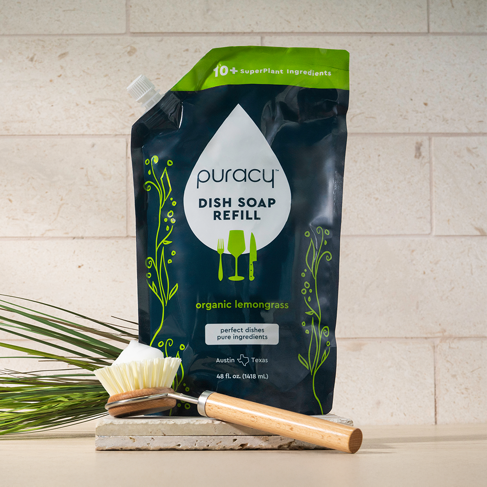 Dish Soap refill pouch with wooden dish brush on counter in front of a tiled wall.