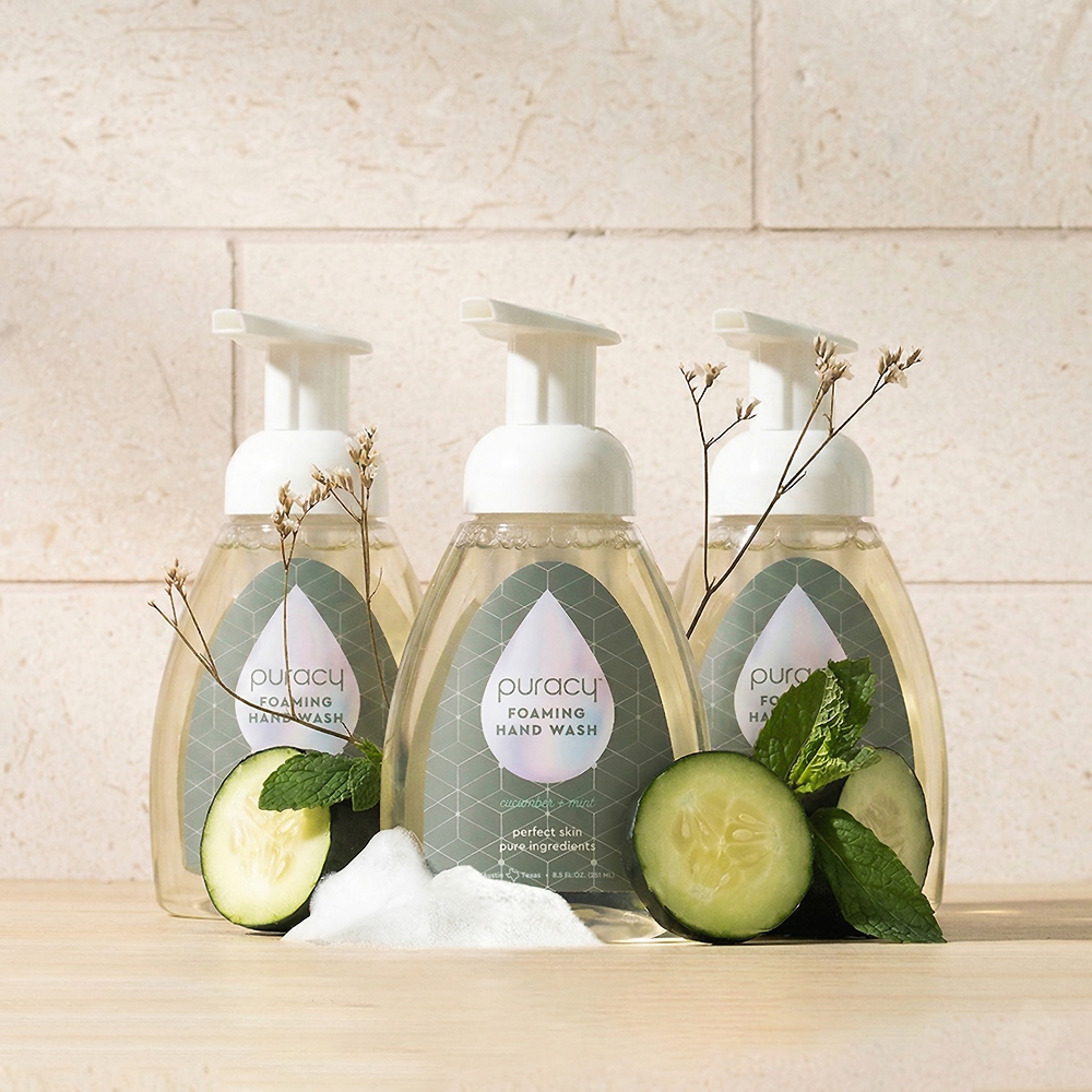 Three bottles of Foaming Hand Soap in cucumber and mint scent on a wooden surface.