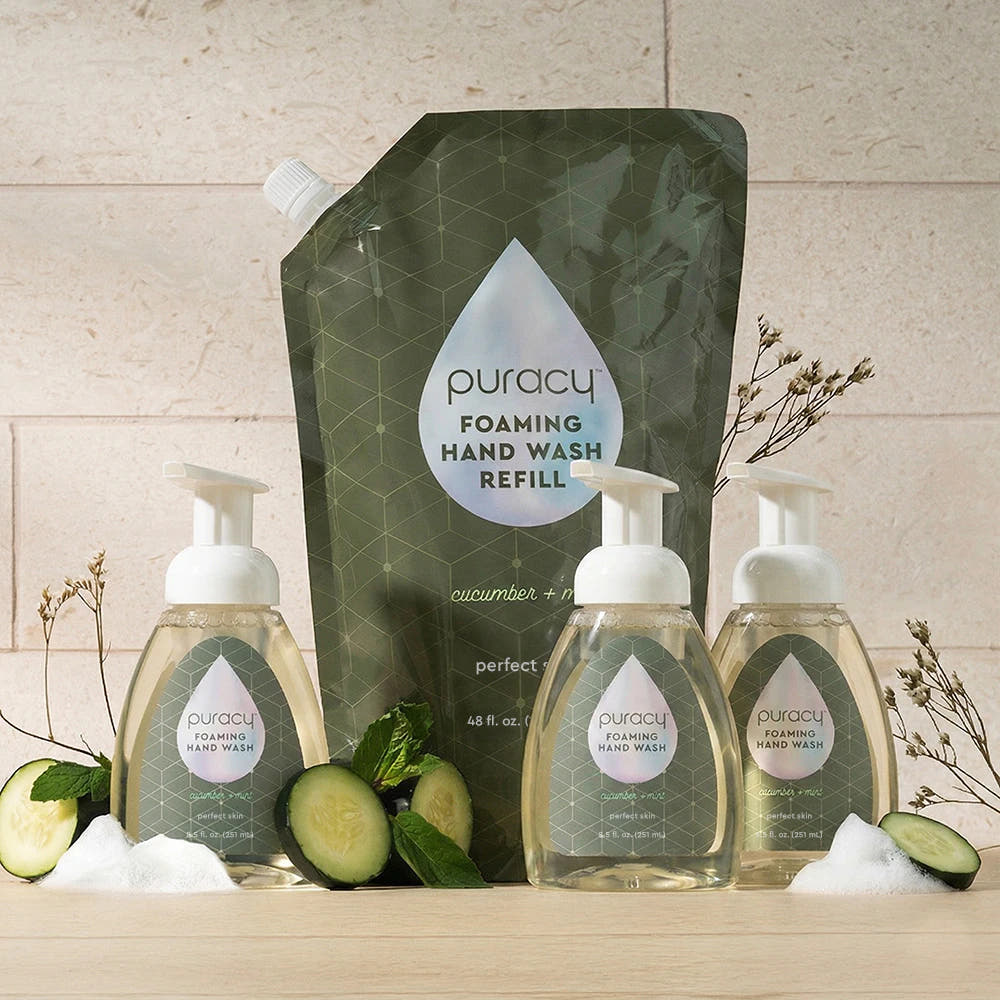 Puracy Foaming Hand Soap bottles and refill, with cucumber slices and foam on a wood surface.