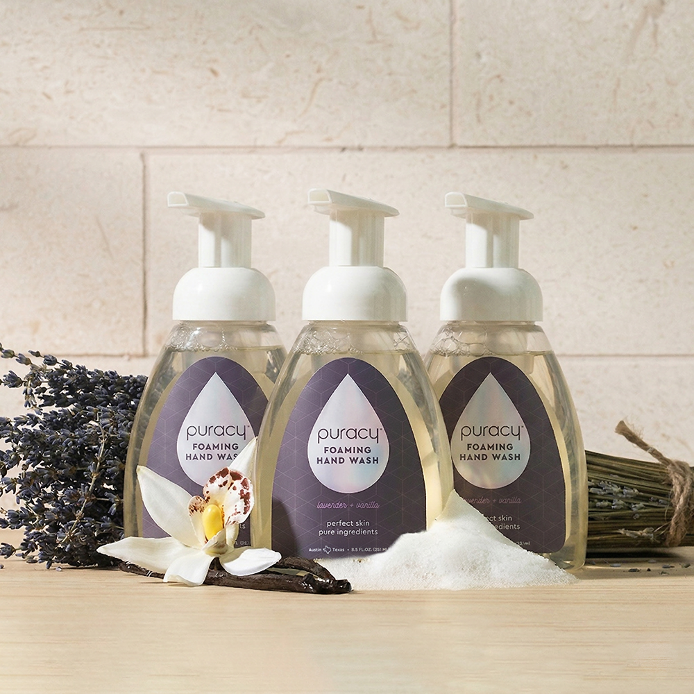 Three bottles of Foaming Hand Soap in lavender, orchid, and soap scents on a wooden surface.