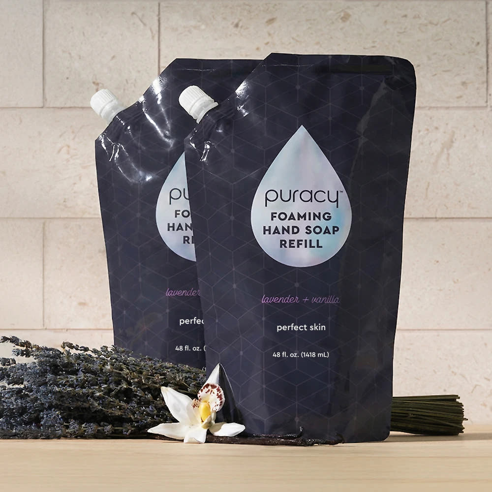 Two Foaming Hand Soap refill pouches with lavender, vanilla flower, and stems beside them.