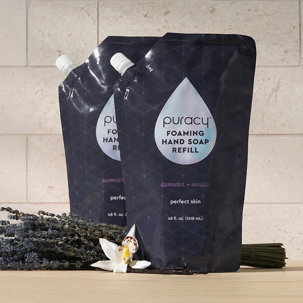 Two Foaming Hand Soap refill pouches with lavender, vanilla flower, and stems beside them.