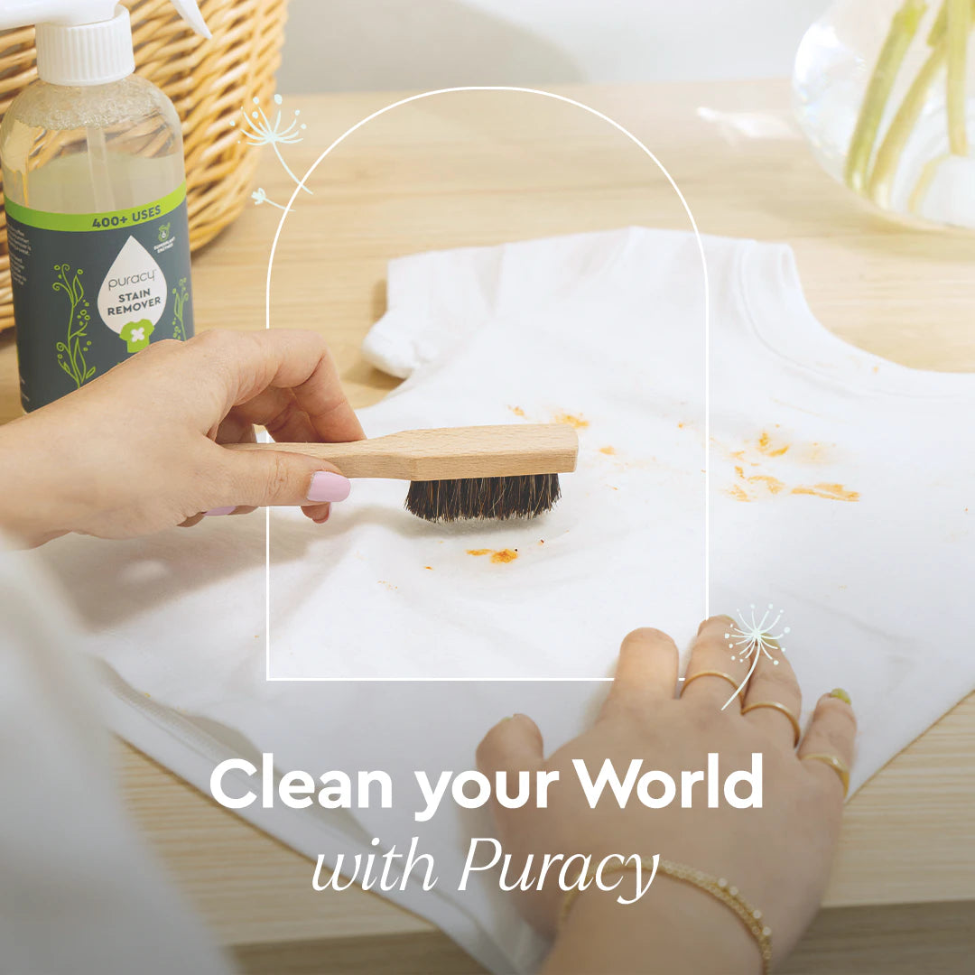 Person cleaning a white shirt with a brush on a wooden table, with Puracy cleaning product visible.