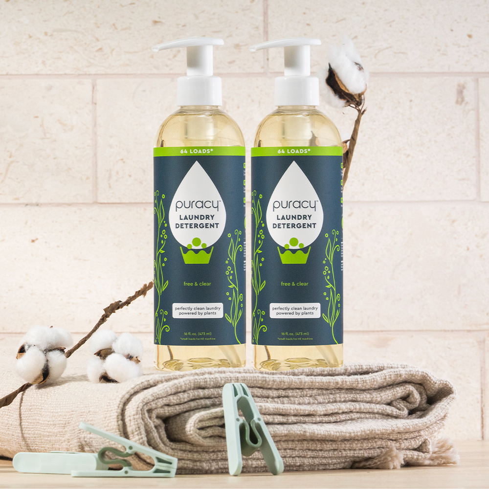 Two bottles of concentrated, sulfate-free Laundry Detergent on folded towels with cotton flowers and clothespins.