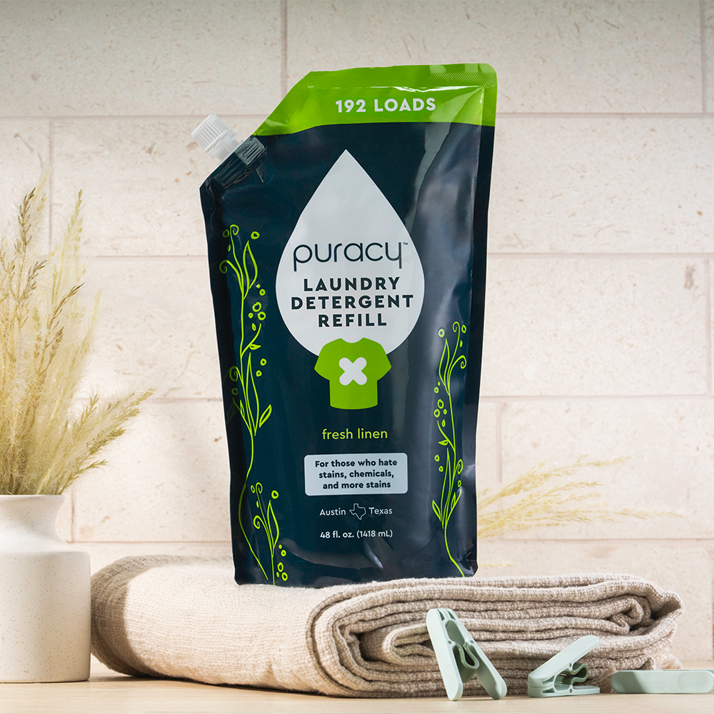 A Laundry Detergent (Concentrated, Sulfate-Free) refill pouch on folded towels with clothespins and a vase.