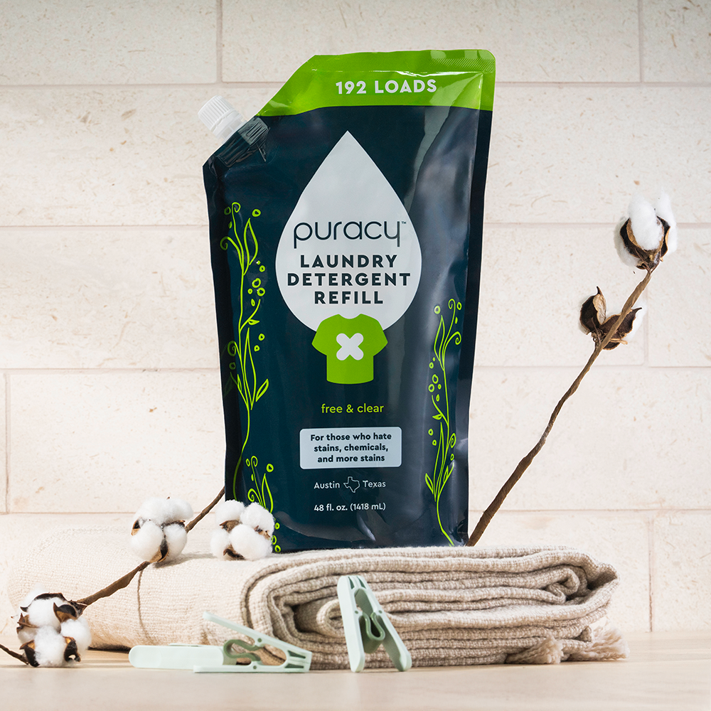 A pouch of concentrated, sulfate-free Laundry Detergent sits on folded towels with cotton branches.