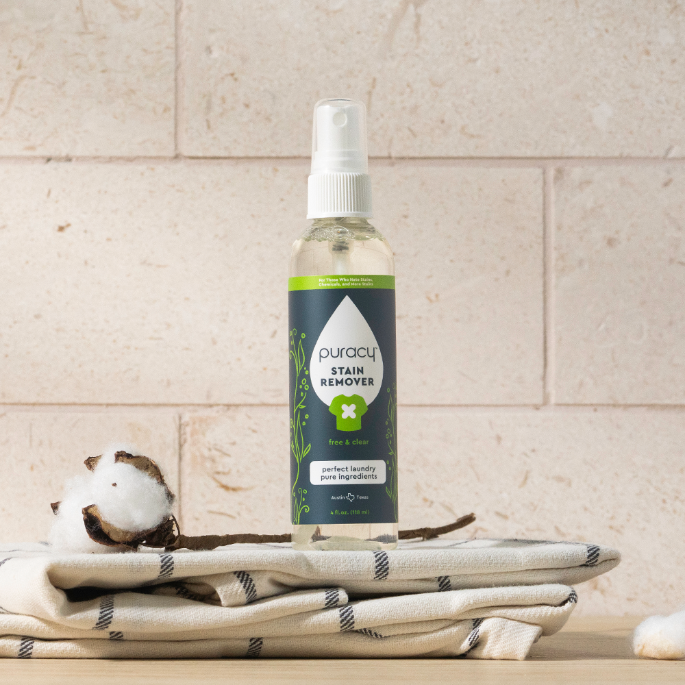 A bottle of Laundry Stain Remover sits on folded cloth and cotton bolls against a tiled backdrop.