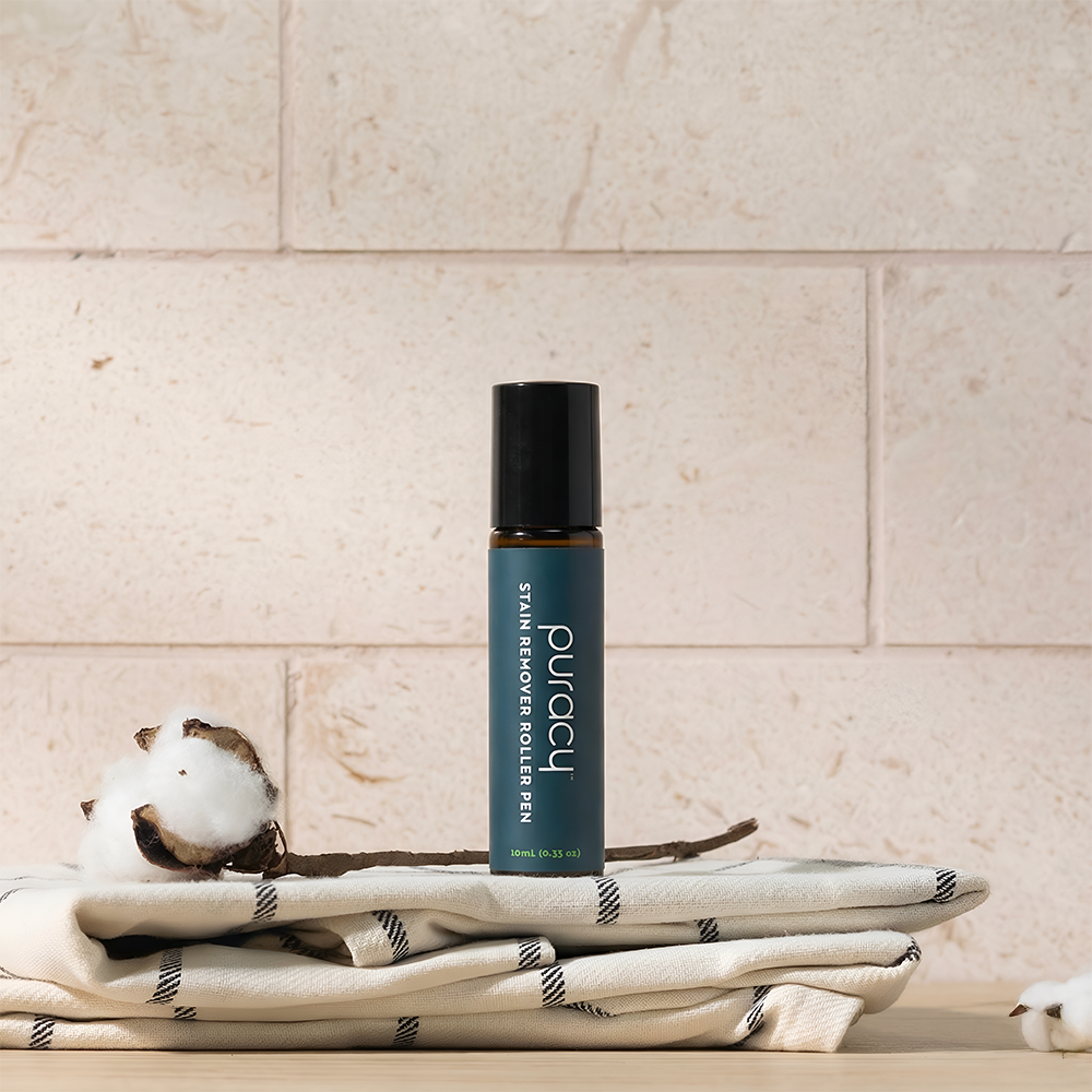 A Laundry Stain Remover bottle sits on a towel with cotton bolls before a beige tiled wall.