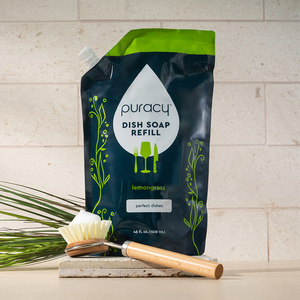 Eco-friendly Dish Soap refill with a dish brush and sponge on a stone surface.