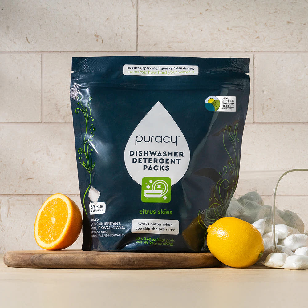 Dishwasher Detergent Pods with citrus and lemon slices on a table, bright neutral background.