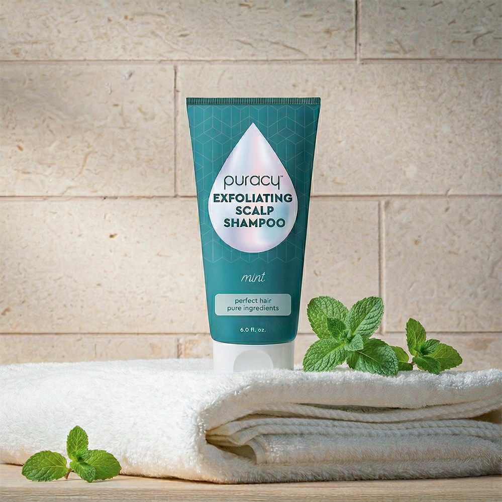 A tube of Exfoliating Scalp Shampoo rests on a towel beside fresh mint leaves.