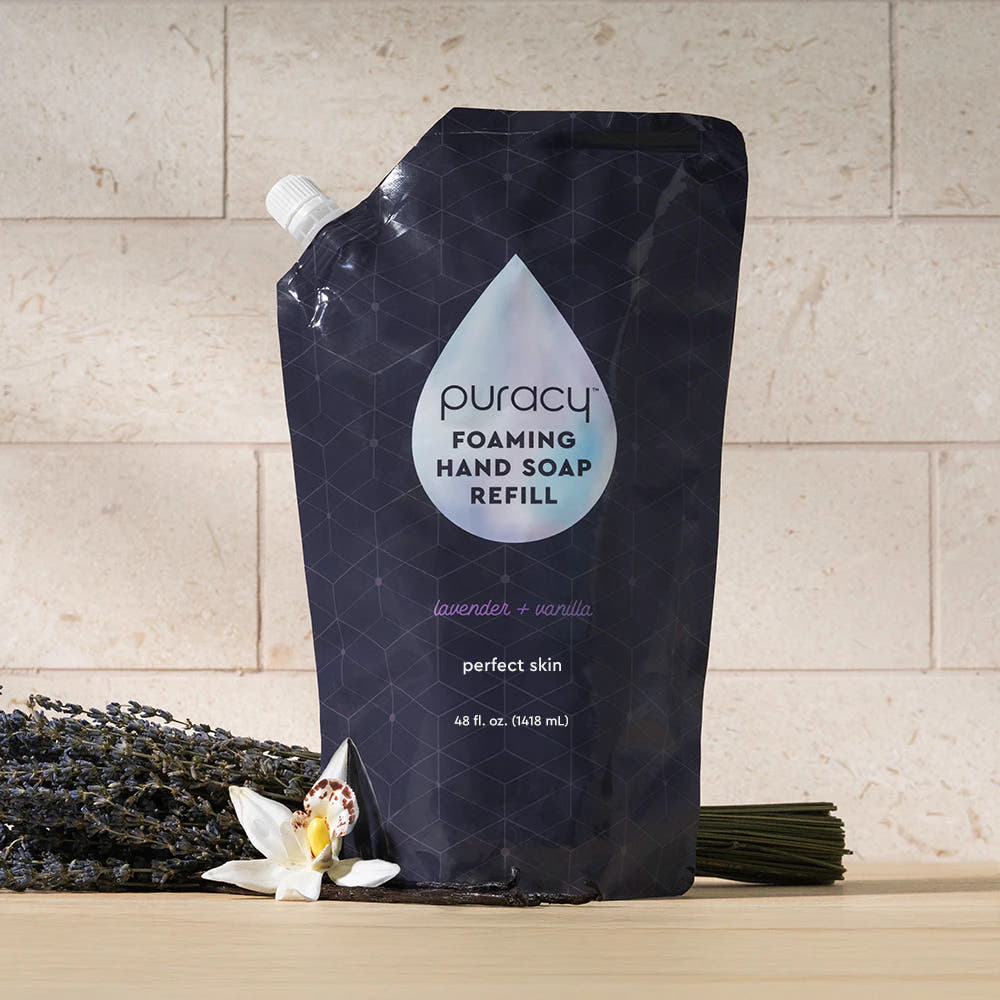 A pouch of Foaming Hand Soap in lavender and vanilla beside lavender and vanilla flowers.