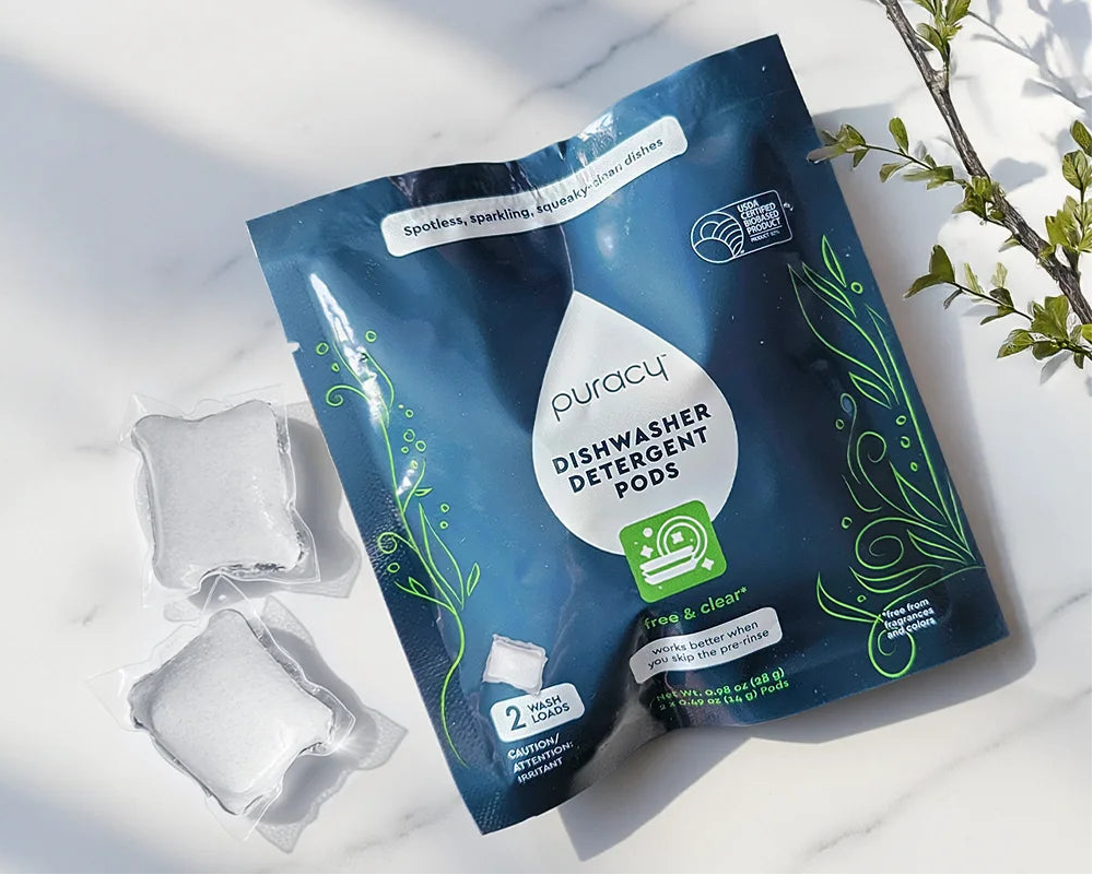 Dishwasher Pods - 2 Satchets (Sample) pack on a white surface, beside a green plant branch.