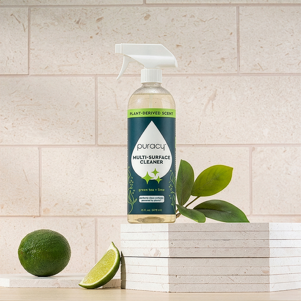 A bottle of Multi-Surface Cleaner Spray with green tea & lime, next to fresh limes.