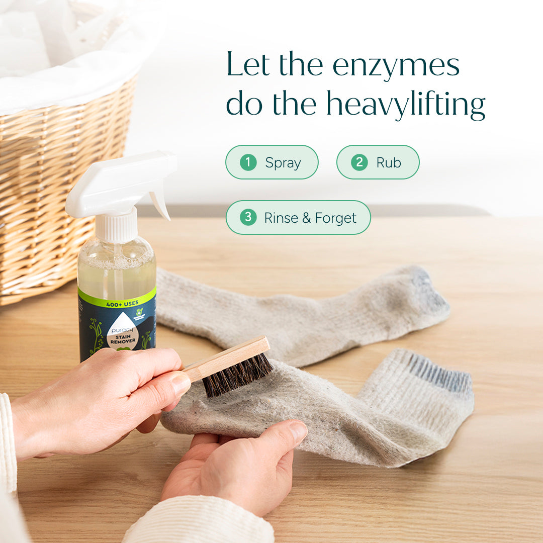 Hands scrubbing a dirty sock with a brush and Laundry Stain Remover - 12oz (Trial Size) on a table.